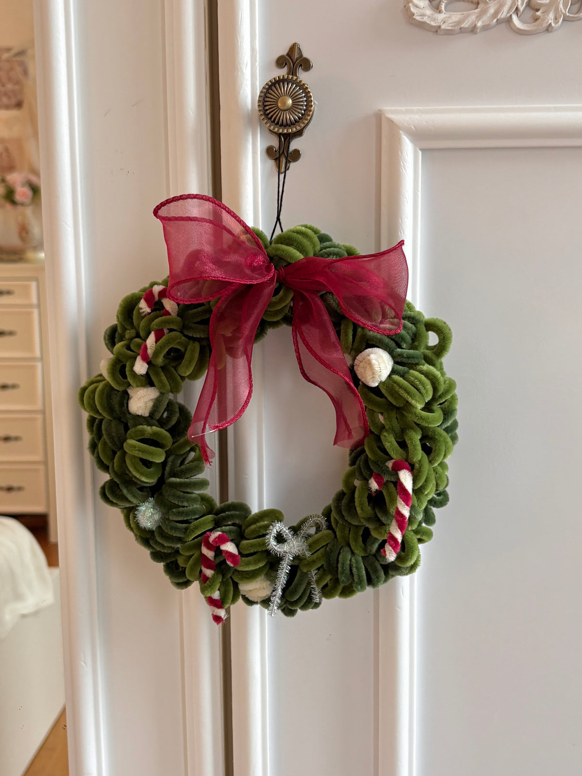 DIY Christmas wreath made from pipe cleaners hanging on a door with a large red bow