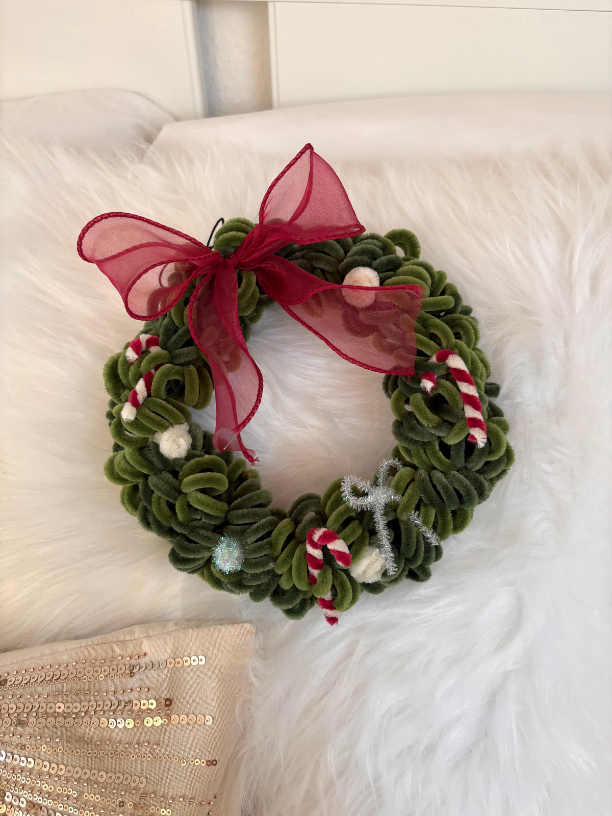 Close-up of a green pipe cleaner Christmas wreath decorated with a red bow and festive accents